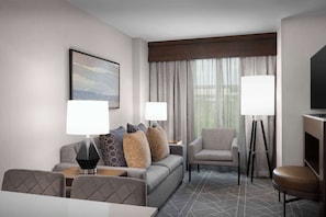 A hotel room with a sofa, armchair, dining table, and a TV.
