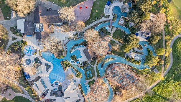 Luchtbeeld van een resort met meerdere zwembaden, een grote windturbine en een kronkelende weg.