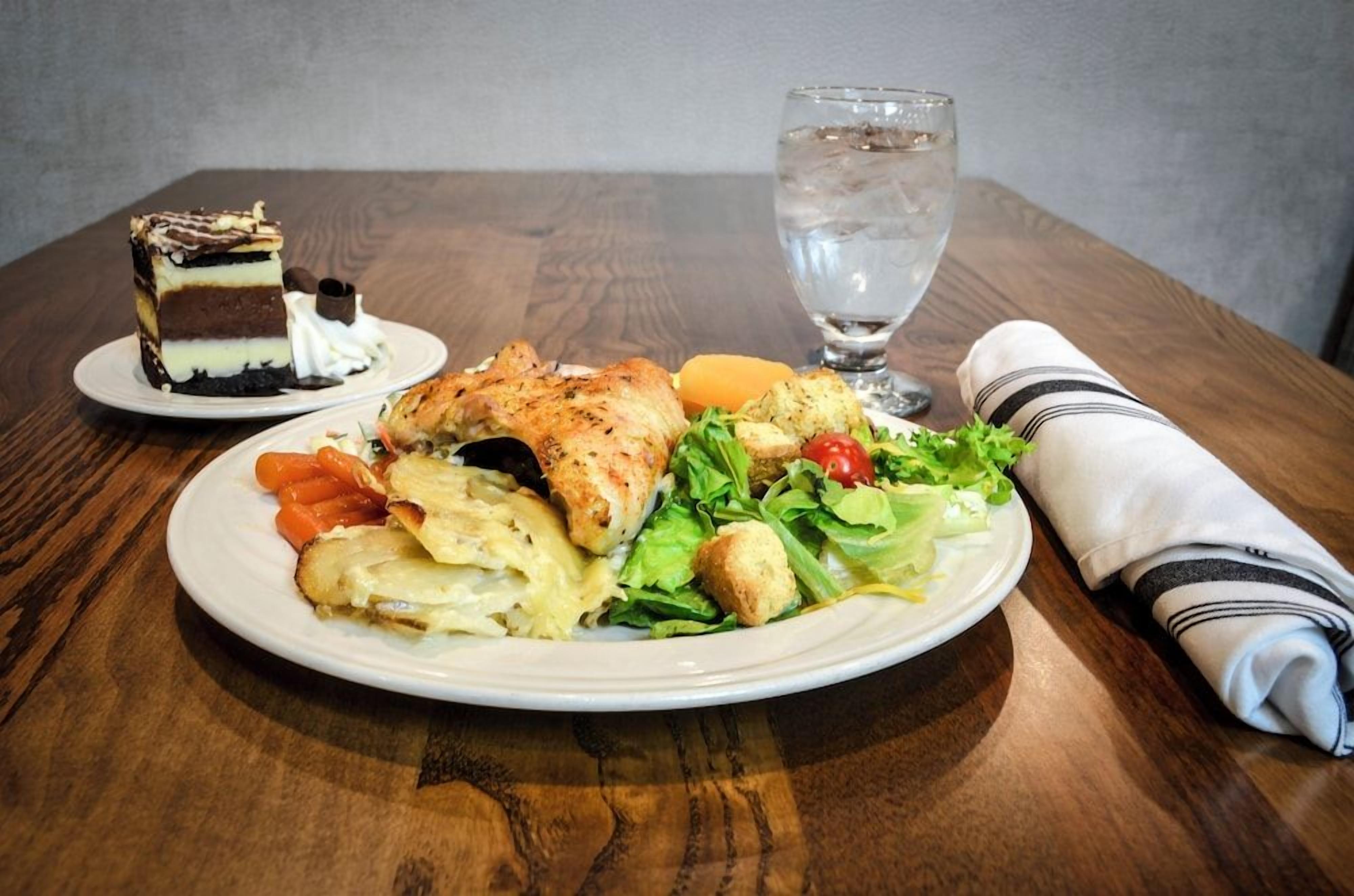 Un repas composé d’une salade, de poulet grillé et d’une part de gâteau, le tout servi sur une table en bois.