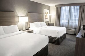 A hotel room with two beds, a desk, a chair, a lamp, and a large window with curtains. - 2 Connecting Suites at a  Hotel (Fargo)