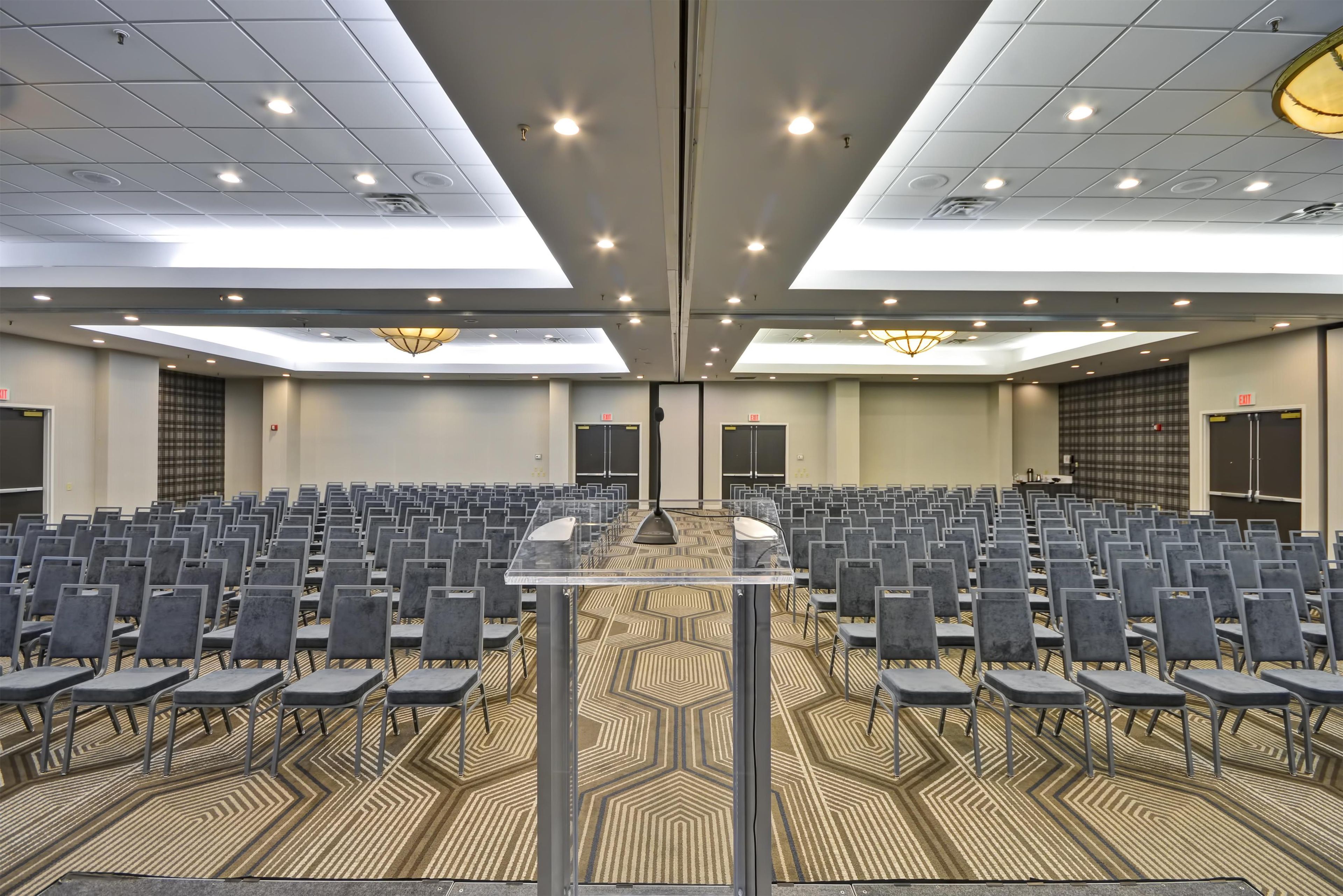 A conference room with rows of chairs, a podium, and a patterned carpet.