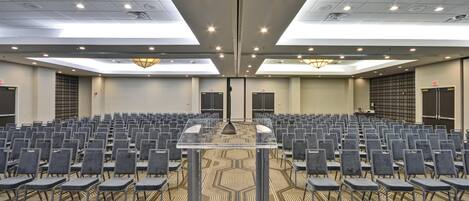 A conference room with rows of chairs, a podium, and a patterned carpet.