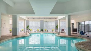 An indoor swimming pool with clear water, surrounded by chairs and potted plants, with a tiled wall and large windows in the background. - 2 Connecting Suites at a  Hotel (Charlotte)