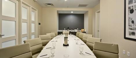 Un salón de conferencias con una larga mesa, sillas y una zona de cocina al fondo.