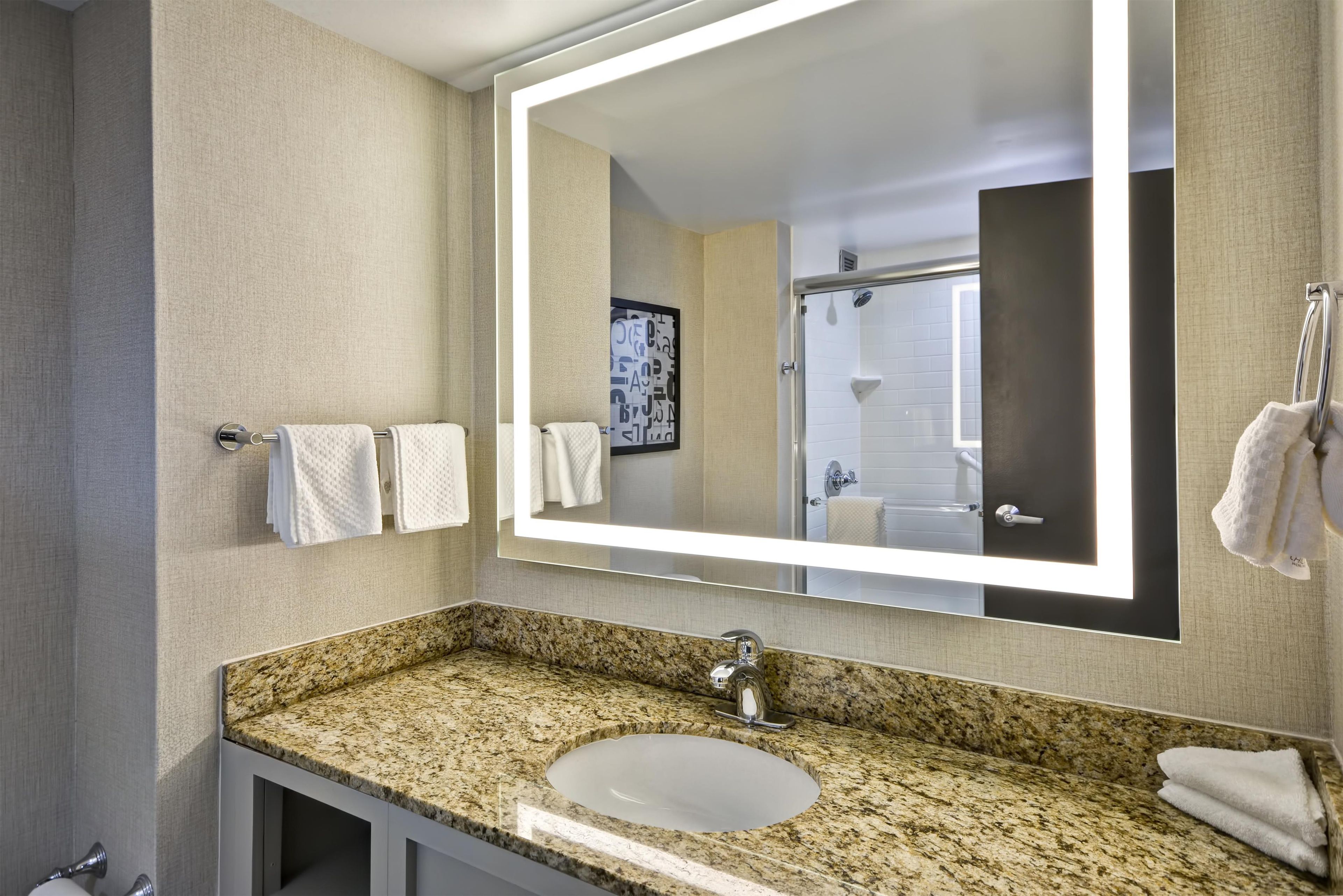 A bathroom with a granite countertop, a white sink, and a large mirror.