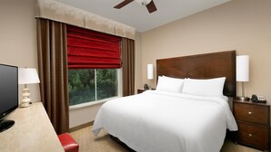 Une chambre d’hôtel avec un grand lit, un bureau avec une lampe, une télévision et une fenêtre avec des rideaux.