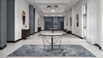 A modern hotel lobby with a central round table, dark patterned rugs, and framed artwork on the walls.