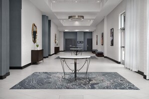 A modern hotel lobby with a central round table, dark patterned rugs, and framed artwork on the walls. - Two King Room at a  Hotel (Birmingham)