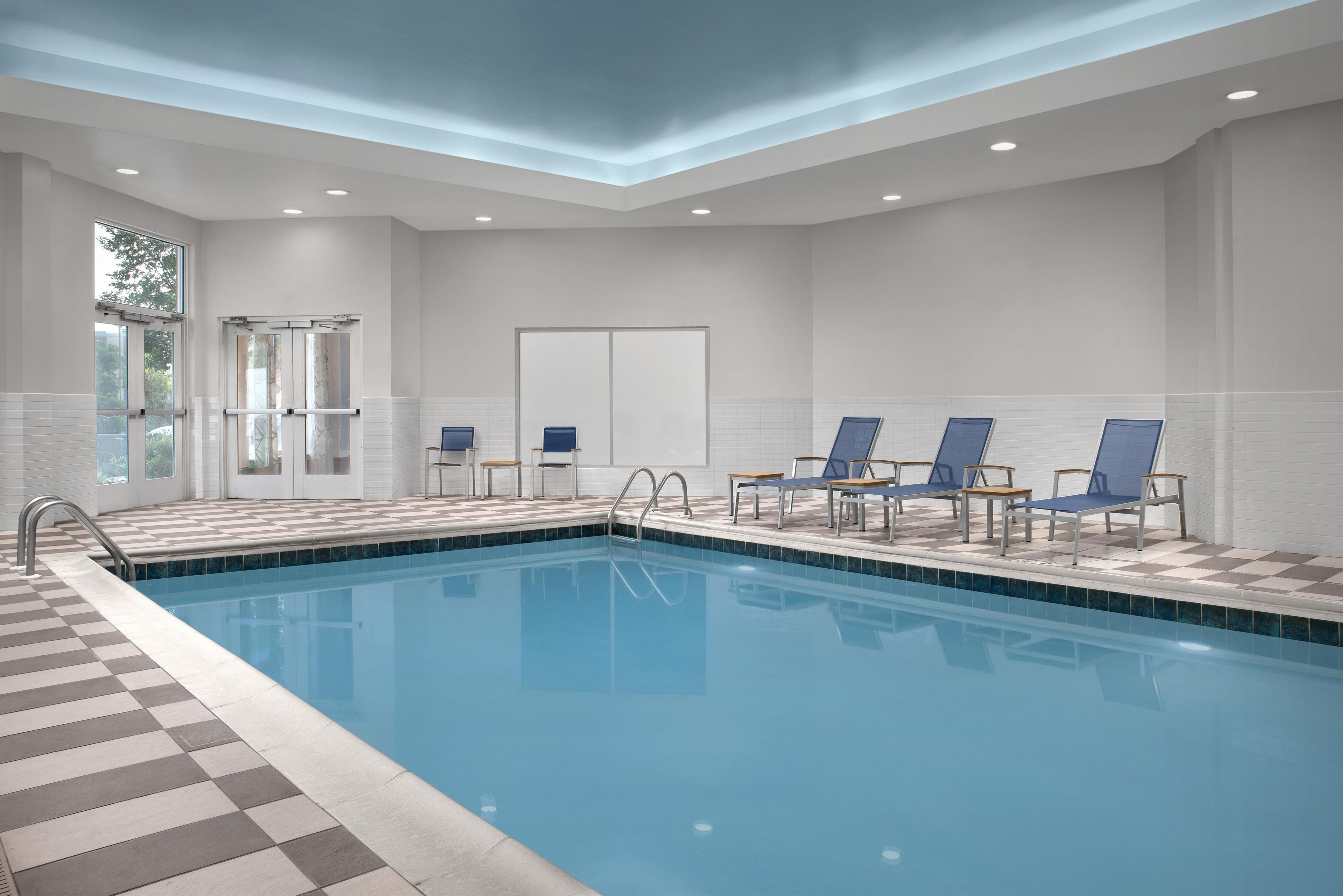 A swimming pool with a checkered border, surrounded by lounge chairs and a door with glass panels.