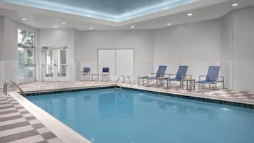 A swimming pool with a checkered border, surrounded by lounge chairs and a door with glass panels.