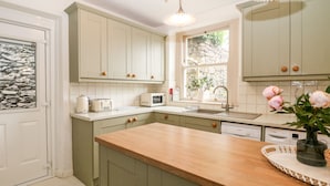 A kitchen with light green cabinets, a wooden countertop, a window with a view, and a hanging light fixture. - Eastview (Matlock)
