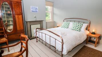 A bedroom with a metal-framed bed, a wooden chair, a wooden cabinet with a mirror, and a fireplace.