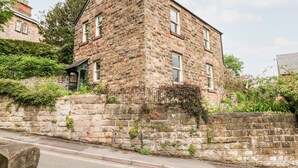 A stone building with a gabled roof, a small porch, and a brick wall with vegetation. - Eastview (Matlock)