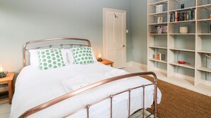 A bedroom with a bed, a bedside table with a lamp, a bookshelf, and a door. - Eastview (Matlock)