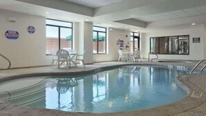 An indoor swimming pool with clear water, surrounded by white chairs and tables.