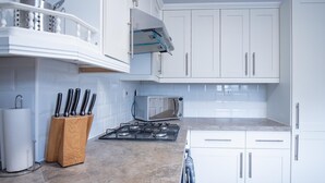 Una cocina moderna con gabinetes blancos, estufa a gas, microondas y un bloque de cuchillos.