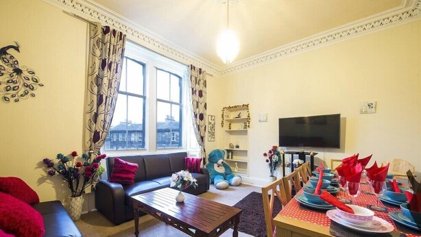 A living room with a sofa, coffee table, and dining table set for a meal. - Morrison Central ApartHotel Edinburgh (Edinburgh)