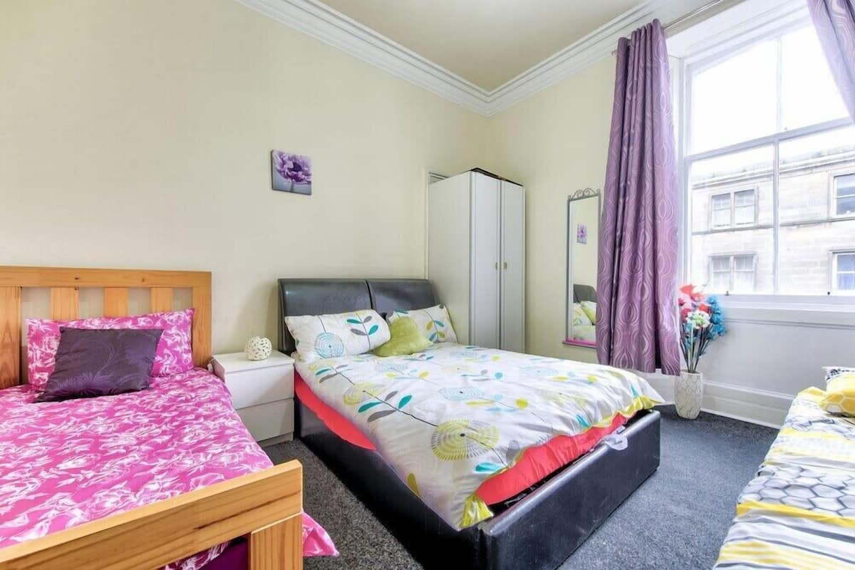 A bedroom with two beds, a wardrobe, a mirror, and a window with curtains.