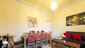 A living room with a dining table set for four, a sofa, a coffee table, and a painting on the wall. - Morrison Central ApartHotel Edinburgh (Edinburgh)