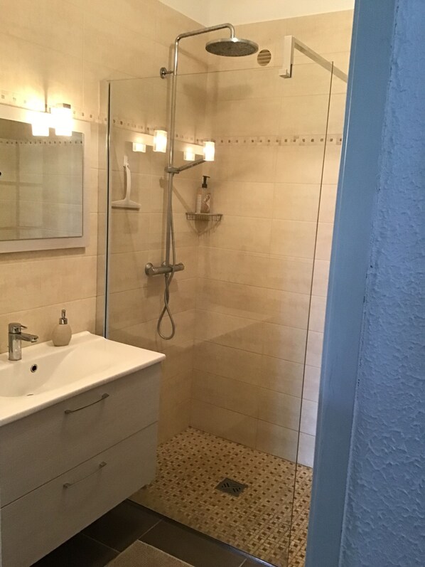 Ein modernes Badezimmer mit einer Duschkabine aus Glas, einem weißen Waschbecken und einem Spiegel.