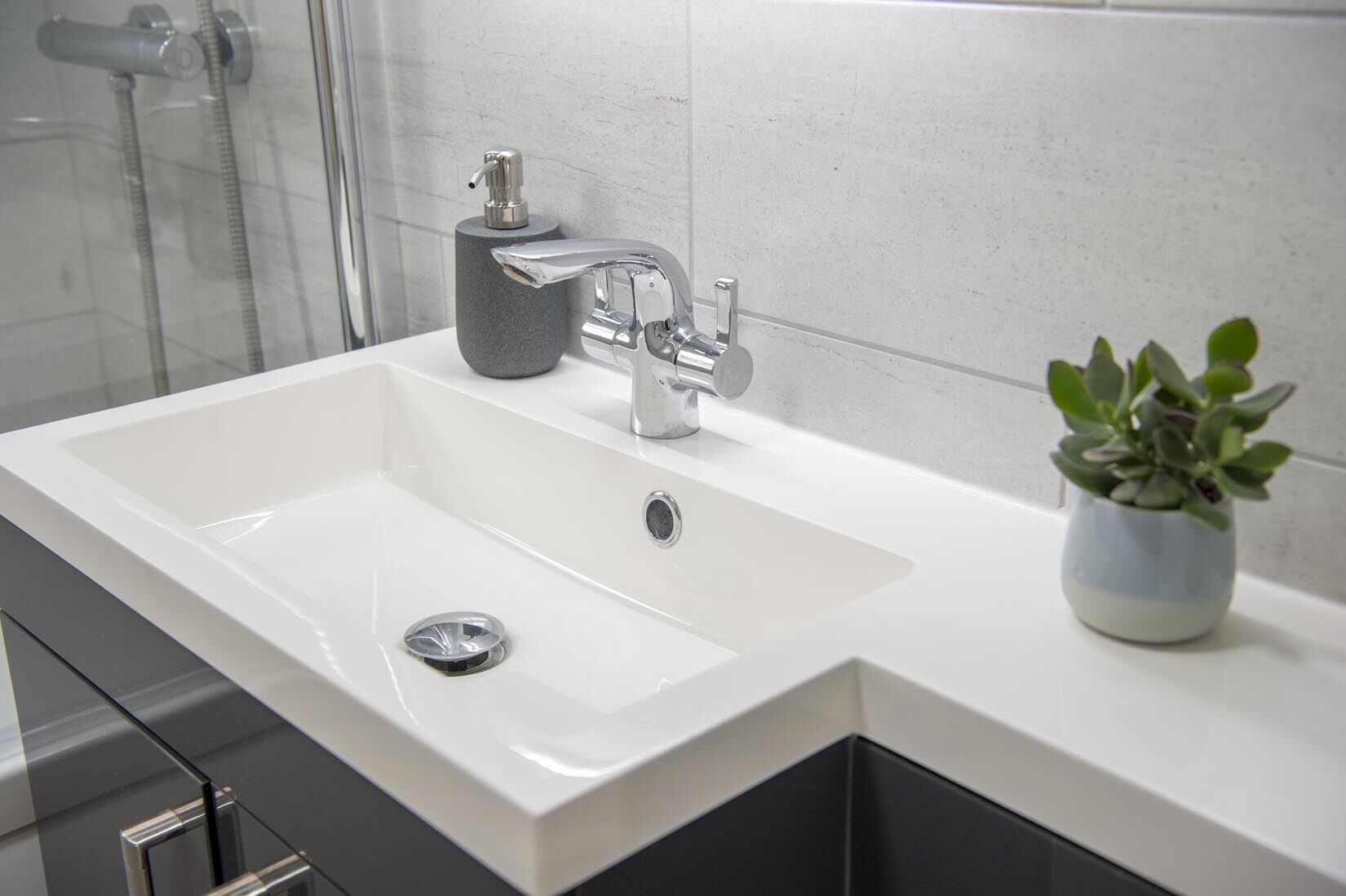 A modern bathroom with a white sink, chrome faucet, and a small potted plant.