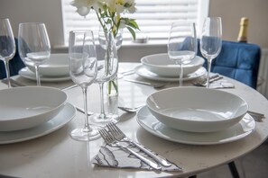 A dining table set with white plates, wine glasses, and silverware, with a vase of flowers in the center. - Penleys Apartment (York)