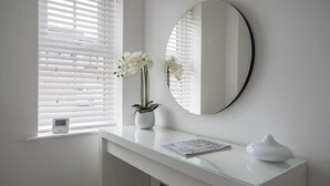 Une salle de bain avec un meuble-lavabo blanc, un miroir rond, une orchidée en pot et un journal posé sur le comptoir.