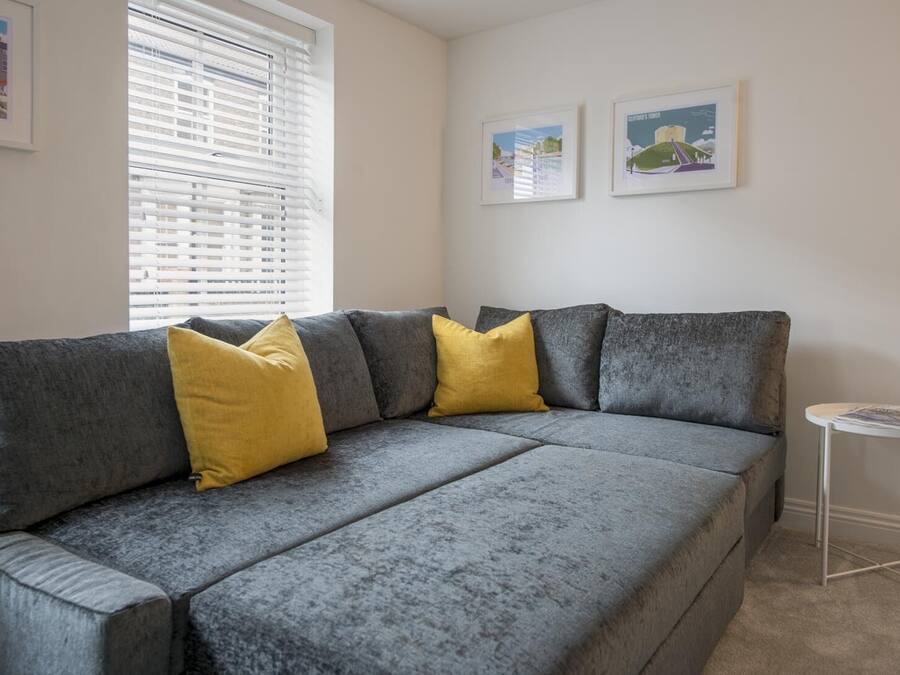 A grey sofa with yellow cushions, a small white side table, and two framed pictures on the wall.