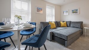 Un salon moderne avec un canapé gris, des fauteuils bleus et une table à manger dressée pour deux personnes.