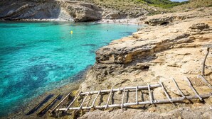 Eine Küstenlandschaft mit klarem türkisblauem Wasser, felsigen Klippen und einer Holzleiter, die ins Wasser führt.