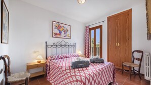Ein Schlafzimmer mit Bett, zwei Nachttischen, einem Sessel, einer Heizung, einem Holzschrank, einem Fenster mit Vorhängen und einem Bild an der Wand.