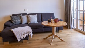 Een kamer met een donkergrijze bank, een ronde houten tafel en een kroonluchter.