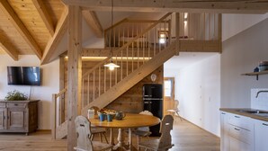 Een houten interieur met een trap, een eettafel met stoelen, een keukenhoek en een flatscreen televisie aan de muur.