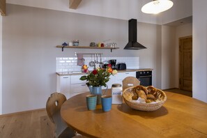 A modern kitchen with white cabinets, a wooden dining table, and a basket of bread. - Ferienwohnung Singer "morgensonne" (Wackersberg)