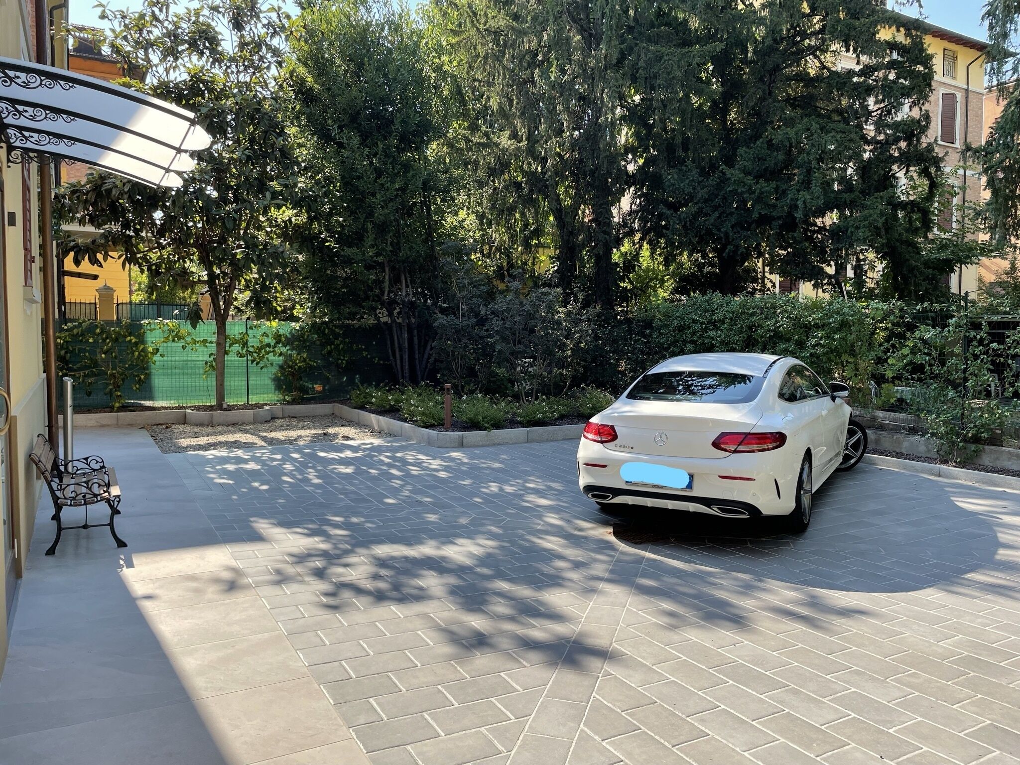 A white car parked in a driveway with a tiled patio and a bench.