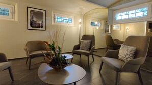 A modern living room with a round coffee table, two armchairs, and a sofa. There are framed pictures on the walls, a window with a view, and a floor lamp. - La Bella Modena Centro (Modena)