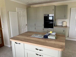 A kitchen with a wooden countertop, a built-in oven, and a small island with a rolled towel and a book.