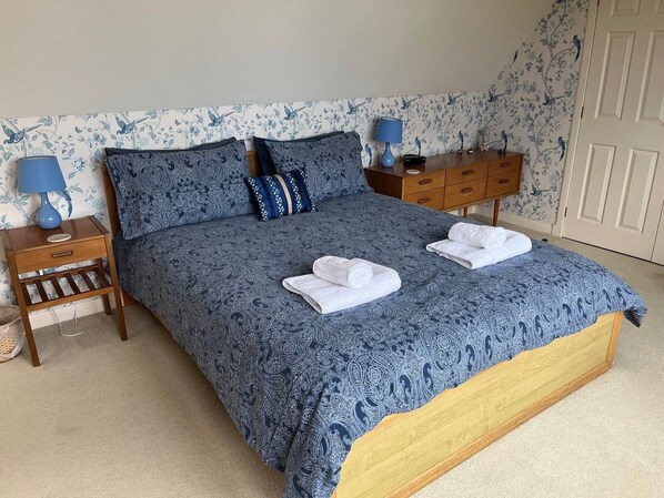 A bedroom with a large bed, two bedside tables, a nightstand, a dresser, and a door.