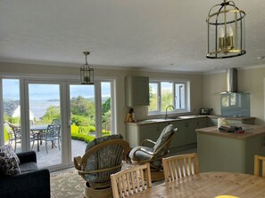 A spacious living area with a view of greenery and a patio, a kitchen with a modern stove, and a dining table with chairs.