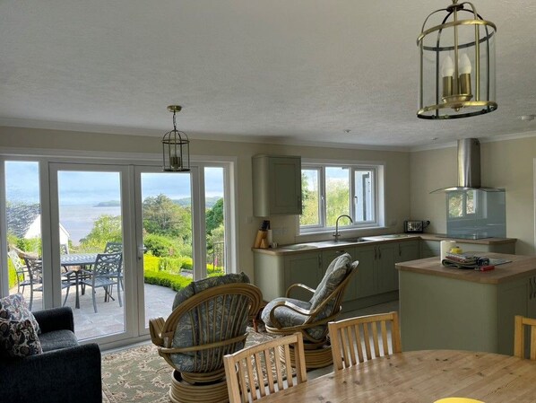 A spacious living area with a view of greenery and a patio, a kitchen with a modern stove, and a dining table with chairs.
