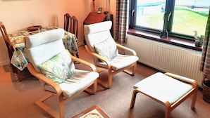 A living room with two armchairs, a small table, and a view of the outdoors through a window.
