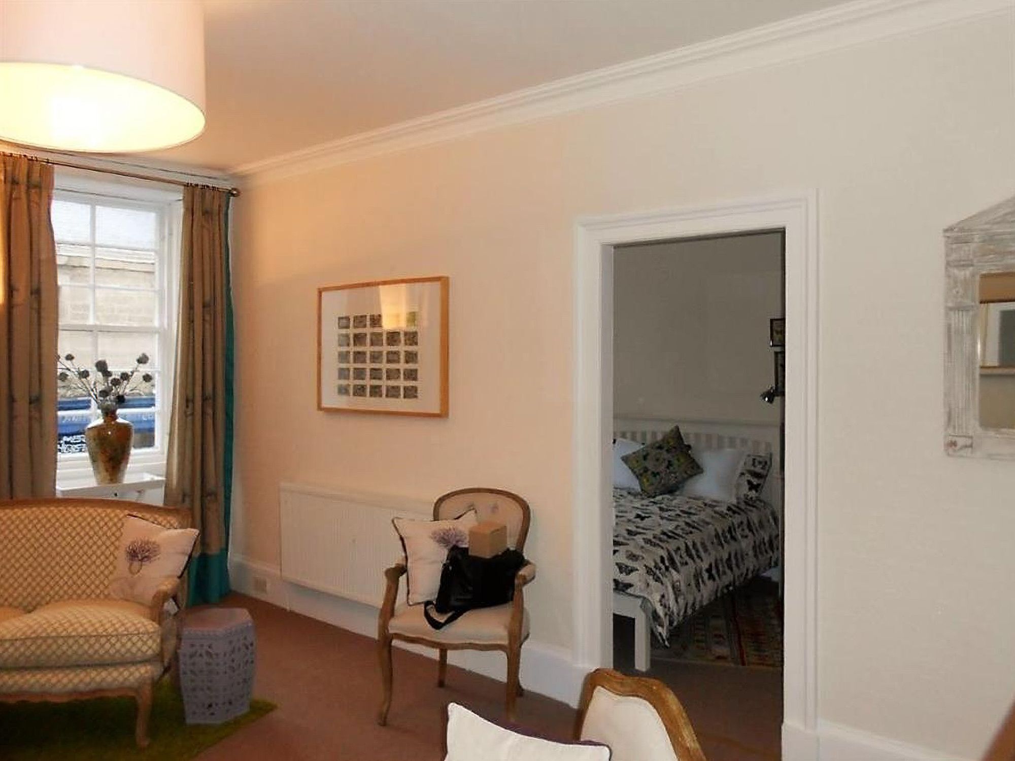 A room with a sofa, a chair, a radiator, a framed picture, and a bed with a patterned bedspread.