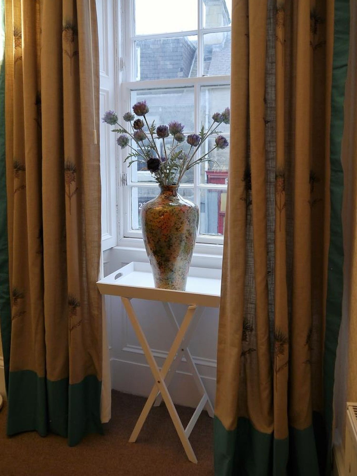 A window with a vase of flowers on a white table.