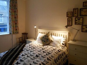 A bedroom with a bed, a nightstand, a lamp, a chair, and a window with curtains.