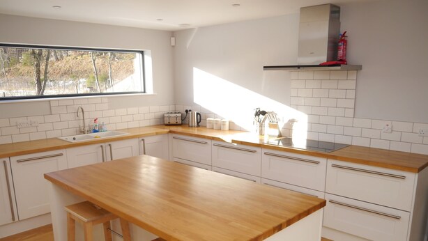 A modern kitchen with white cabinets, a wooden countertop, and a window providing natural light. - Laundry Cottage -  a house that sleeps 8 guests  in 4 bedrooms (Aberlour)