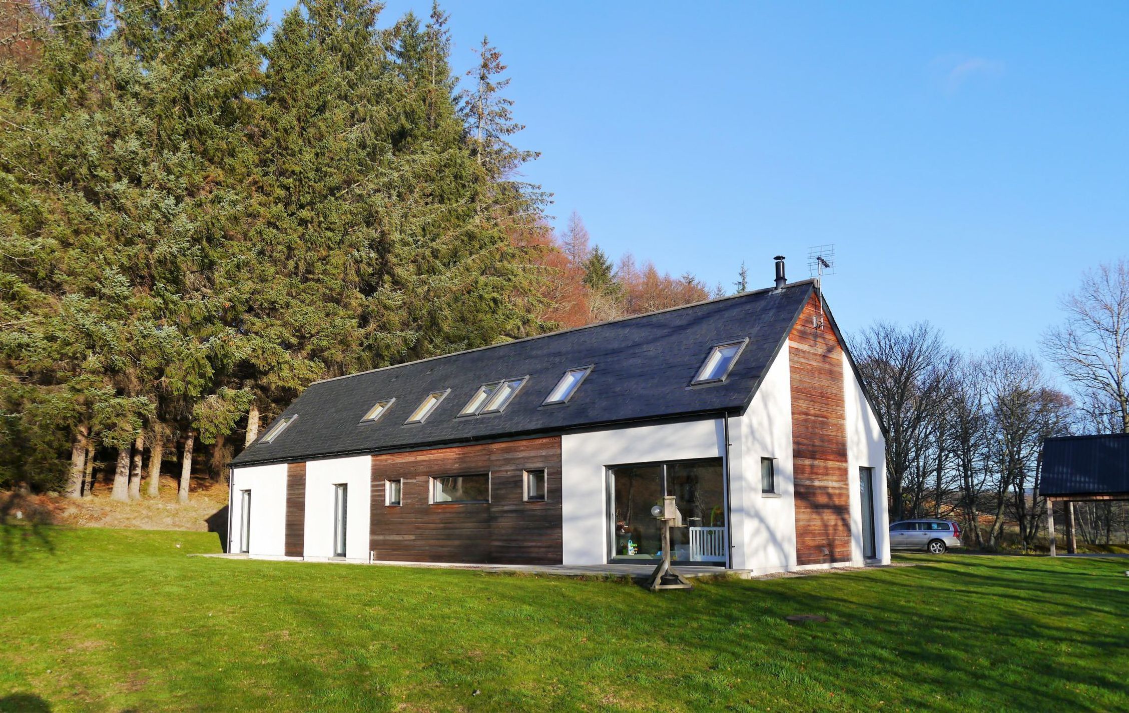 Una casa moderna amb teulada inclinada, finestres grans i façana de fusta.