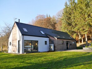 Une maison moderne avec un toit en pente, de grandes fenêtres et une pelouse bien entretenue.