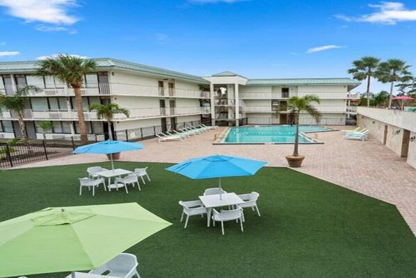 A hotel with a pool, outdoor seating, and palm trees.