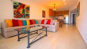 A modern living room with a sofa, colorful cushions, a glass coffee table, and a painting on the wall.