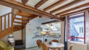 Een keuken met witte kastjes, een houten trap en een eethoek met een ronde tafel en stoelen.